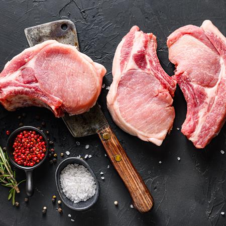 pork chop set on cleaver with rosemary and red pepper on black slate