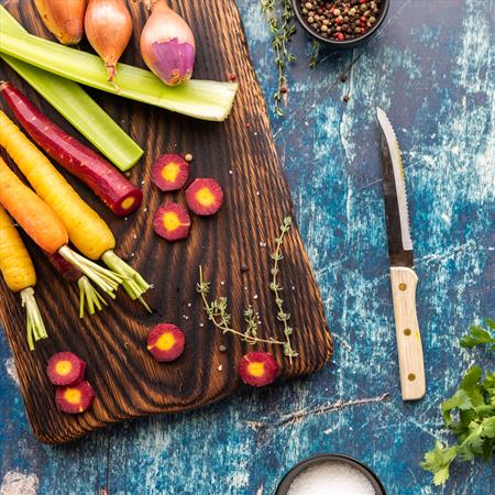 overhead view of a wooden cutting board topped with raw vegetables used in cooking bone broth