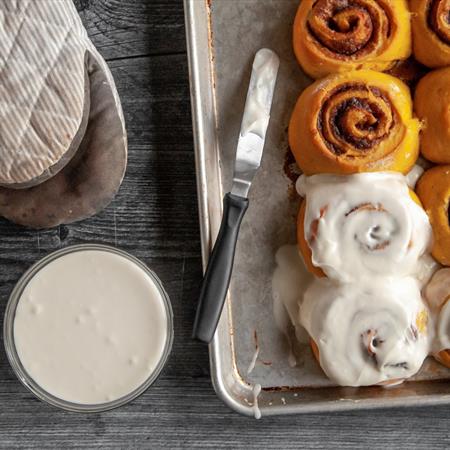 top down view of pumpkin cinnamon roll recipe with two rolls iced on sheet pan