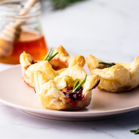 cranberry brie bites on a plate with honey in the background on a white countertop
