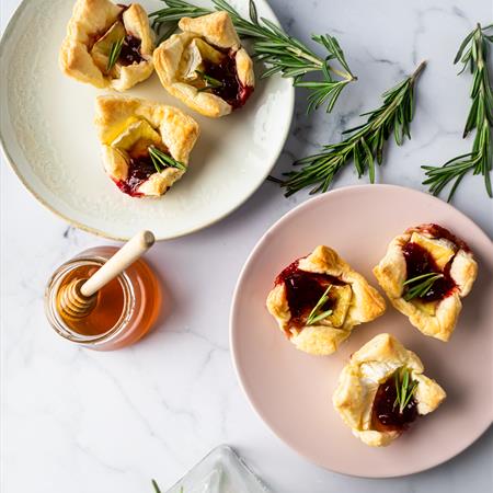 two plates of finished baked brie cranberry honey bites on a white background taken from above