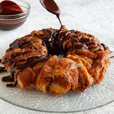 chocolate sauce being drizzled over doughnut monkey bread recipe on white countertop